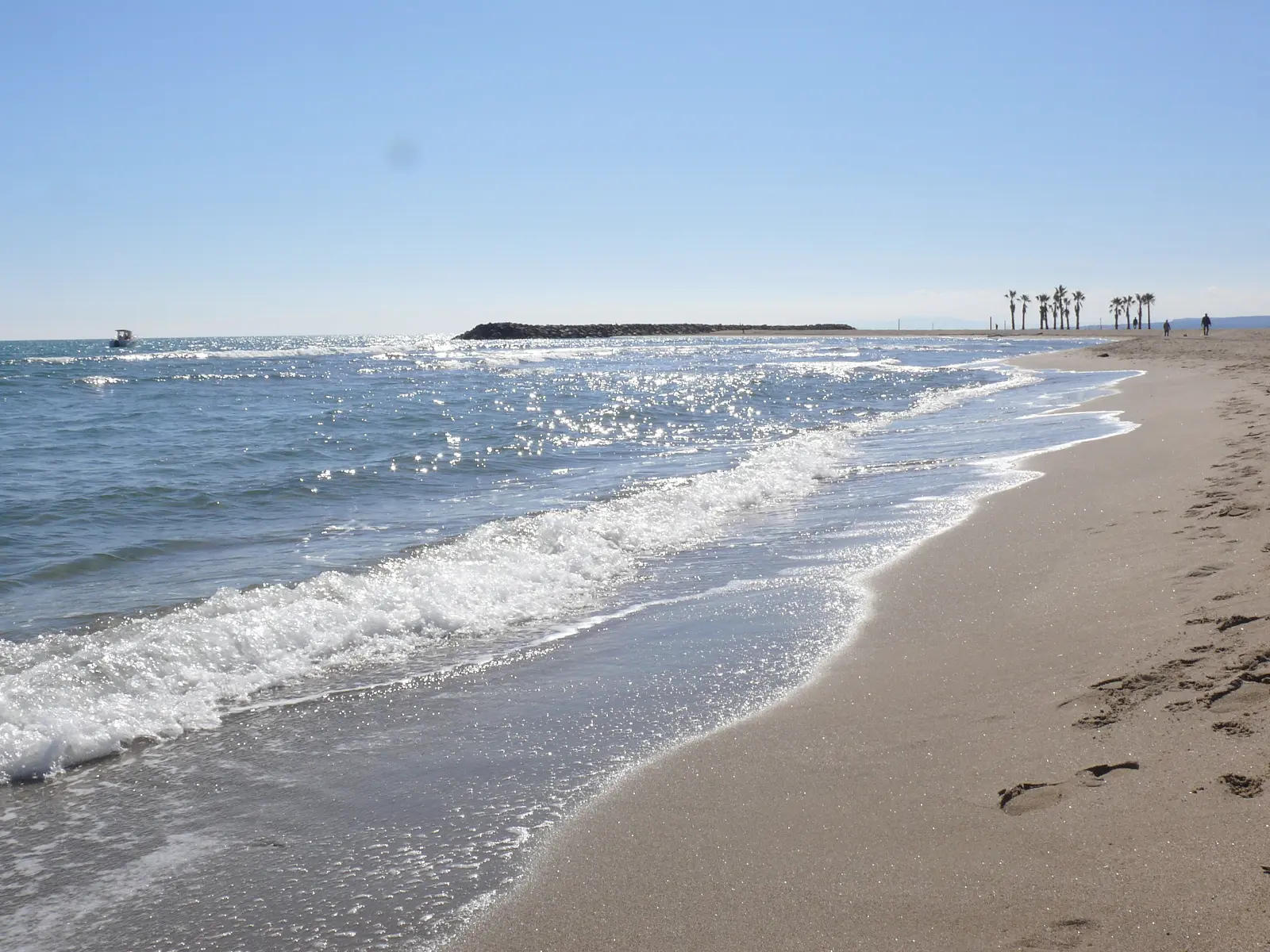 Sable fin et mer sous ciel bleu avec quelques nuages blancs
