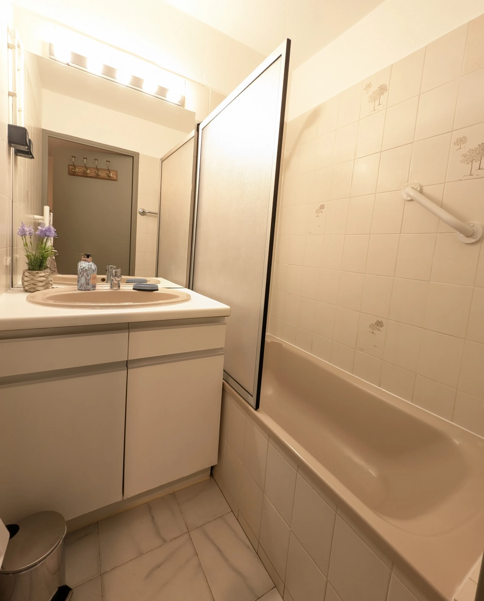 Salle de bain rose beige clair avec baignoire, pare-douche et poignée de sécurité